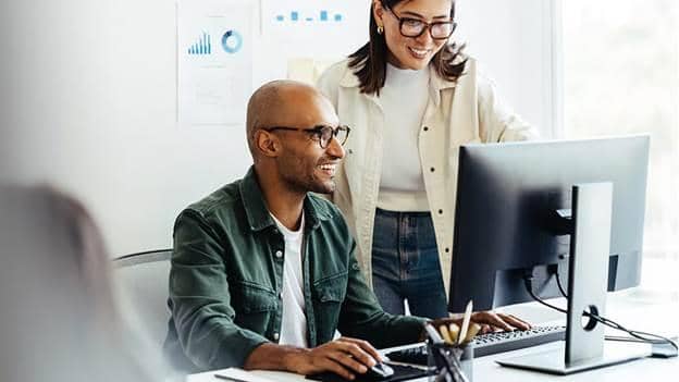 Two colleagues review sales performance charts together at an office computer.